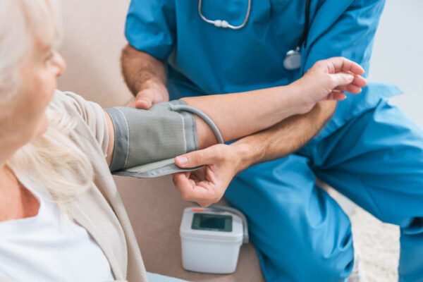 cropped shot of caregiver measuring blood pressure to senior woman