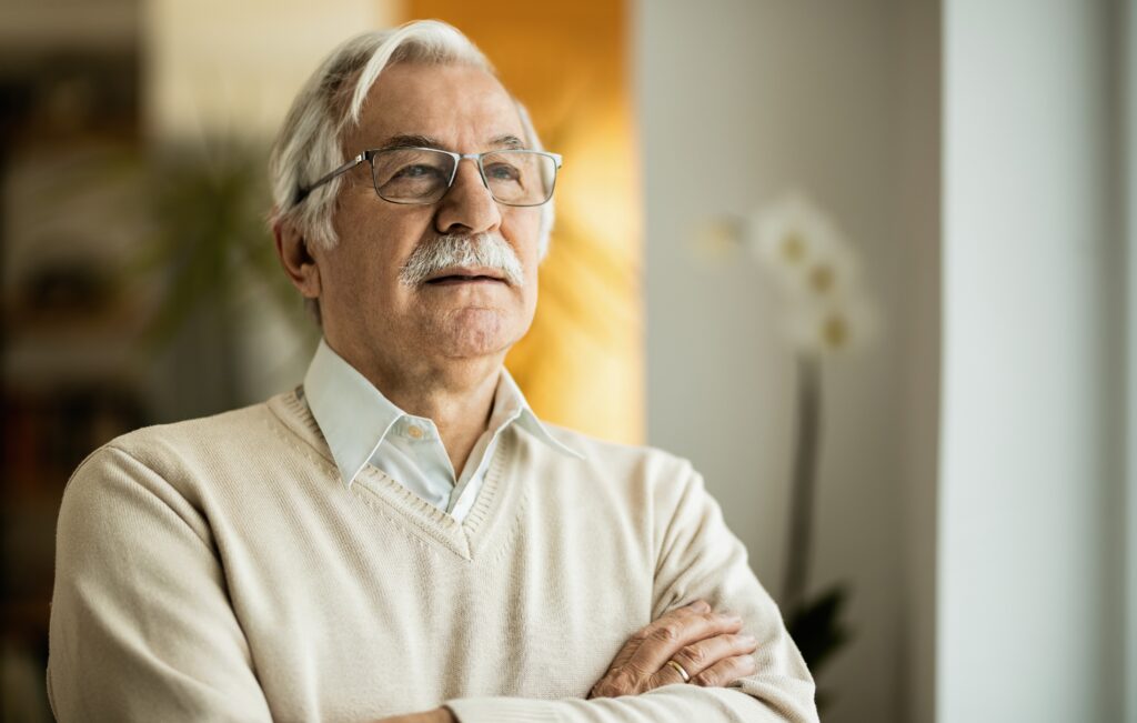 Portrait of pensive senior man day dreaming at home.